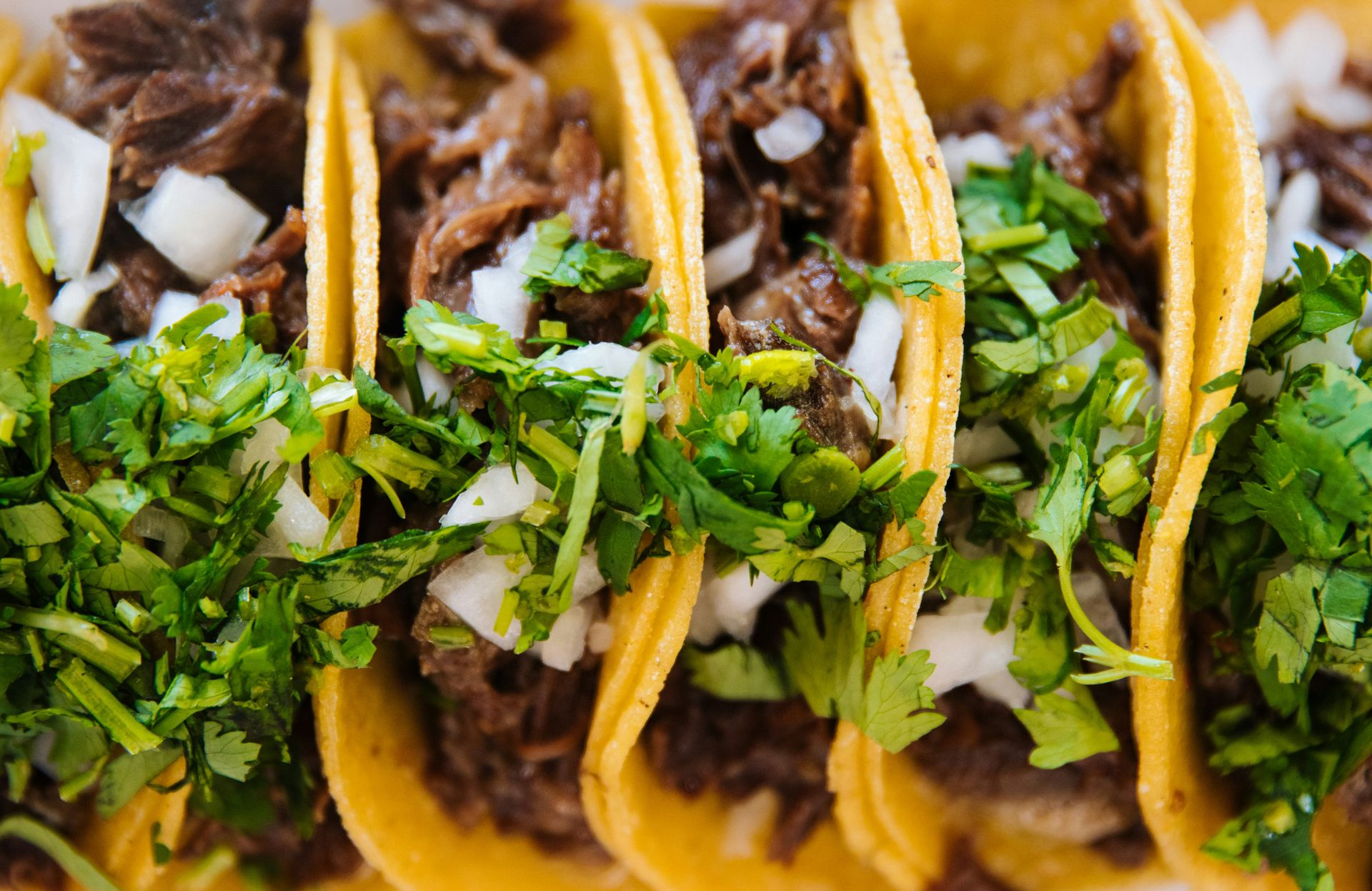 Three beef tacos topped with chopped white onions and fresh cilantro